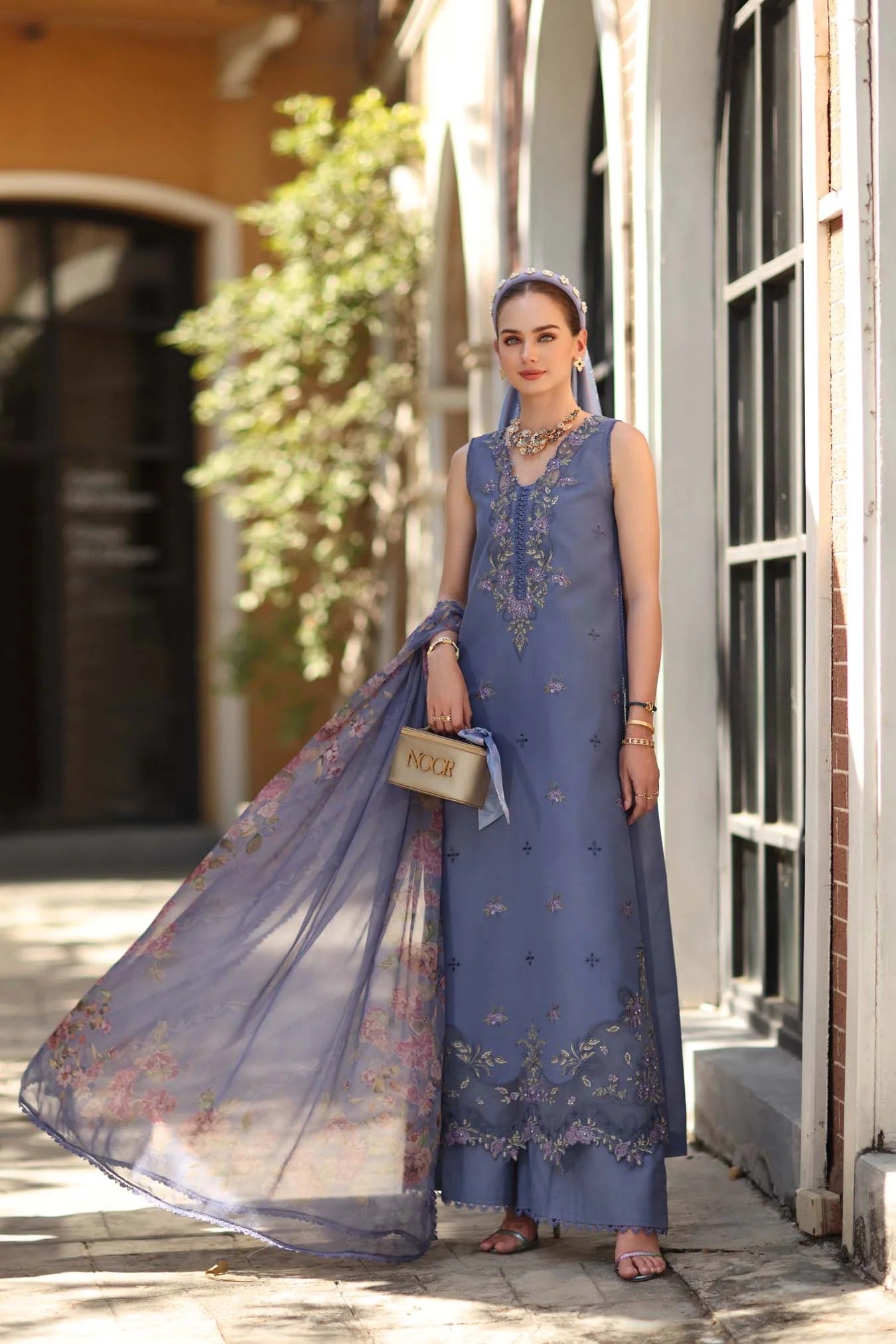 Woman in a blue embroidered dress with a floral dupatta standing outdoors.