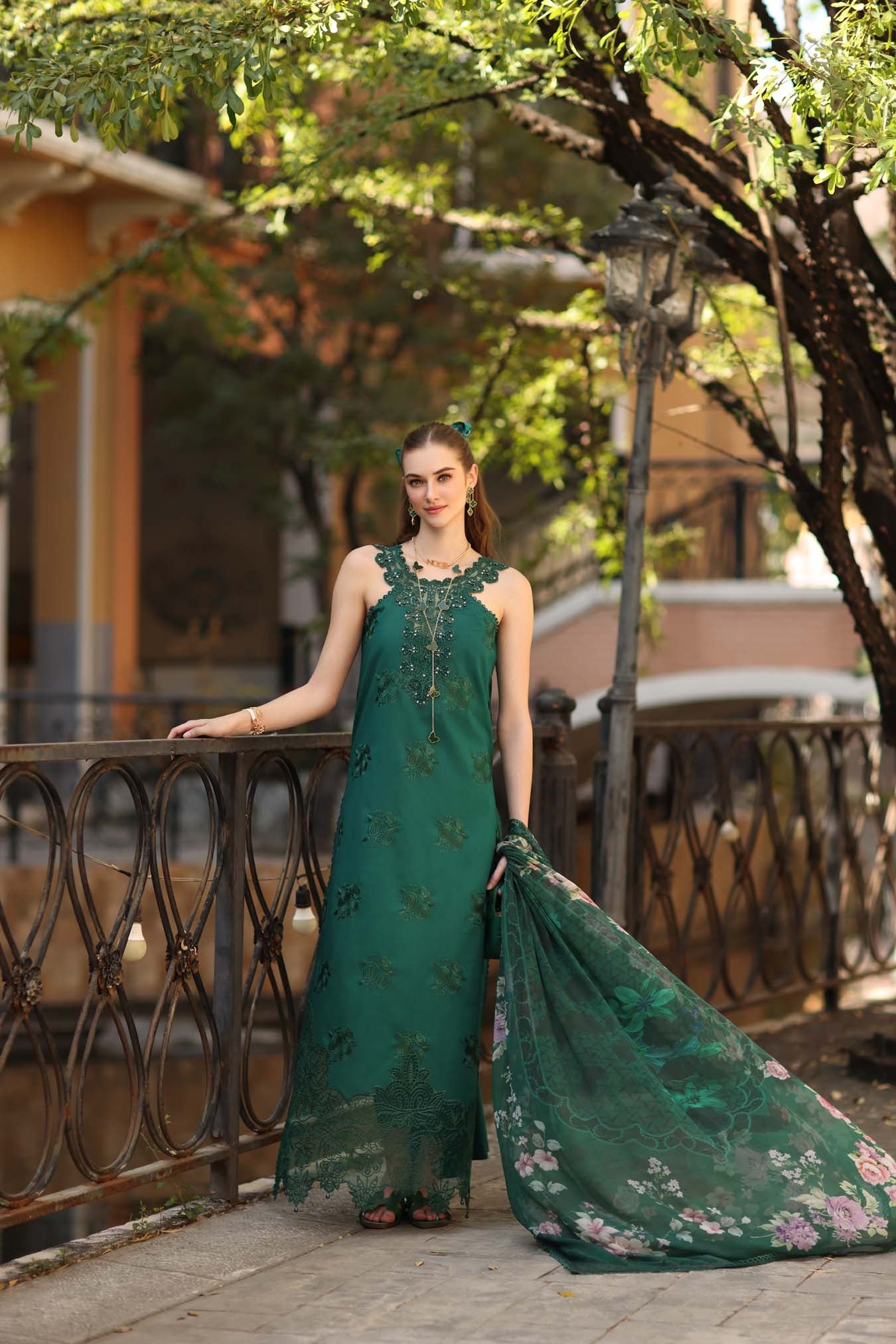 Woman in a green dress with floral patterns standing outdoors near a railing.