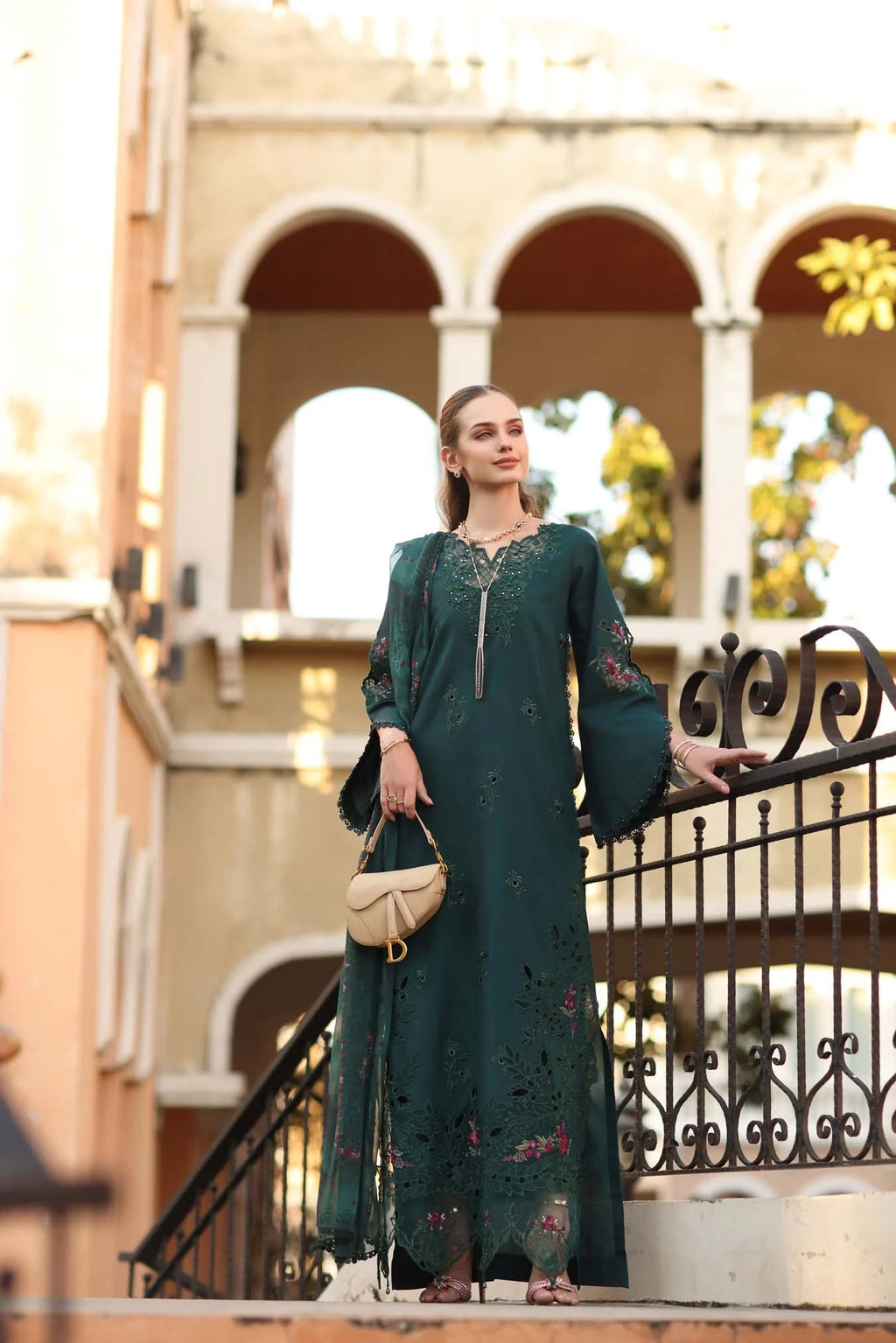 Woman in a green dress standing outdoors with classical architecture in the background