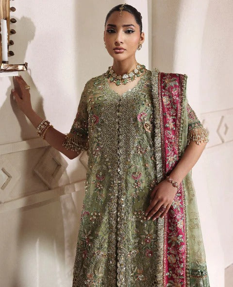 Woman in a traditional embroidered outfit with a pink border against a white wall.