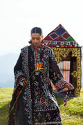 Woman in a patterned dress holding a flower in front of a colorful tent.