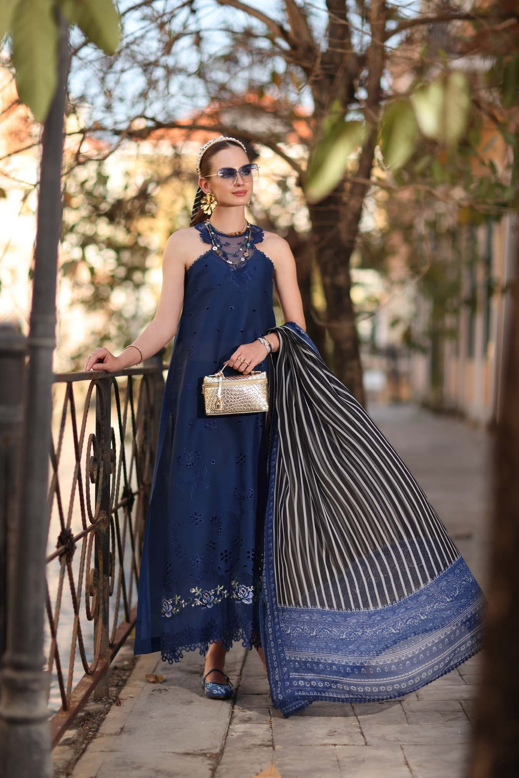 Woman in a blue dress holding a striped shawl outdoors.