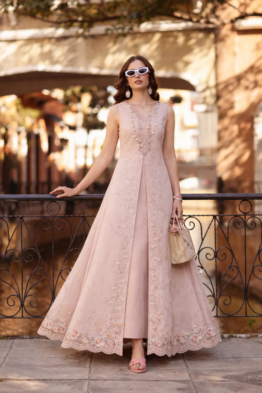 Woman in a long, light pink lace dress standing outdoors with blurred background