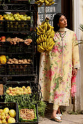 Woman in a floral coat with bananas over her shoulder in front of a fruit stand.