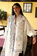 Woman wearing a cream-colored embroidered shirt with a matching shawl in a room.