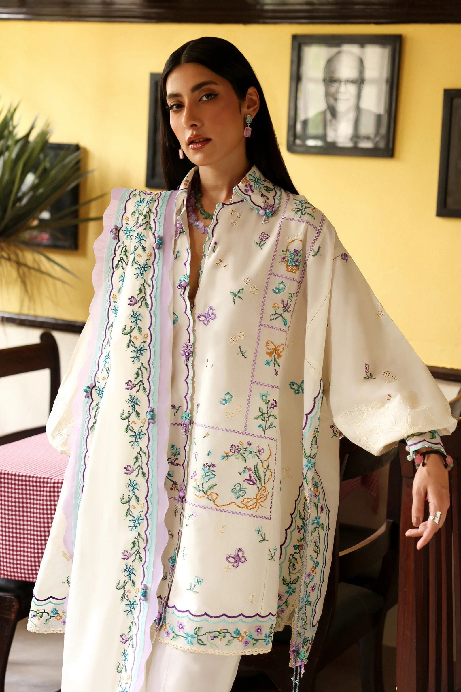 Woman wearing a cream-colored embroidered shirt with a matching shawl in a room.