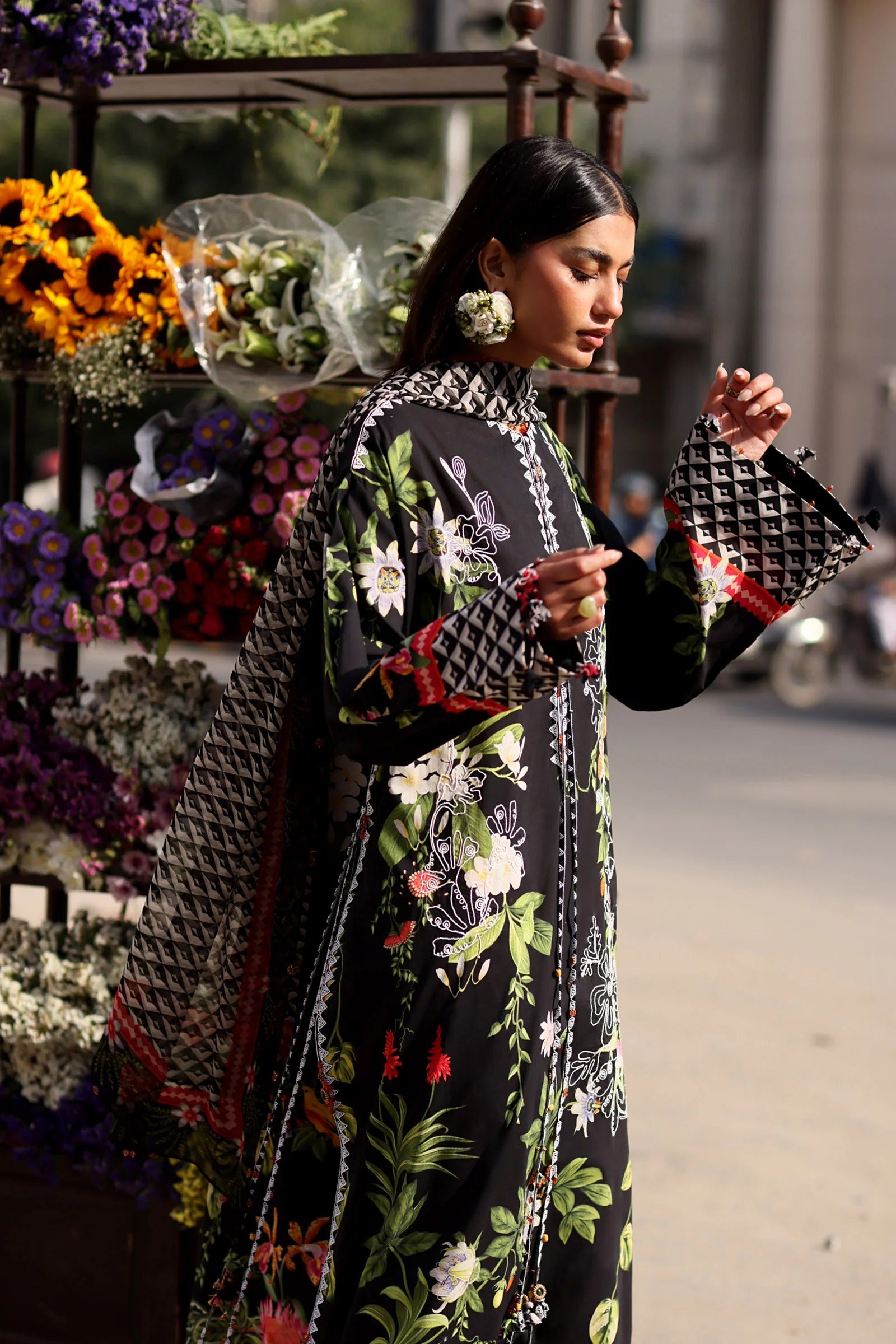 Woman in a floral dress holding a patterned handbag near a flower stand.