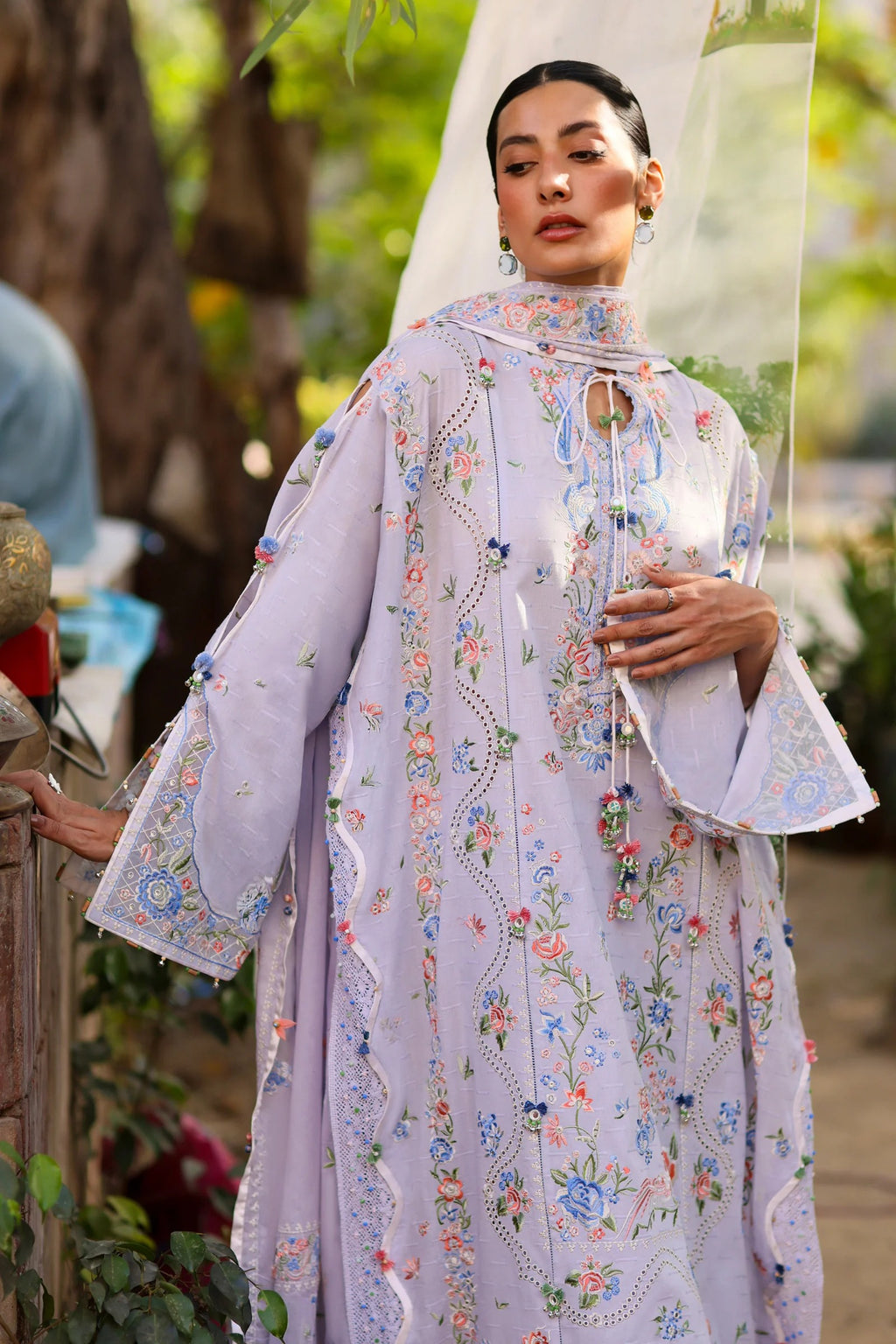 Woman wearing a light purple embroidered traditional outfit with a blurred outdoor background