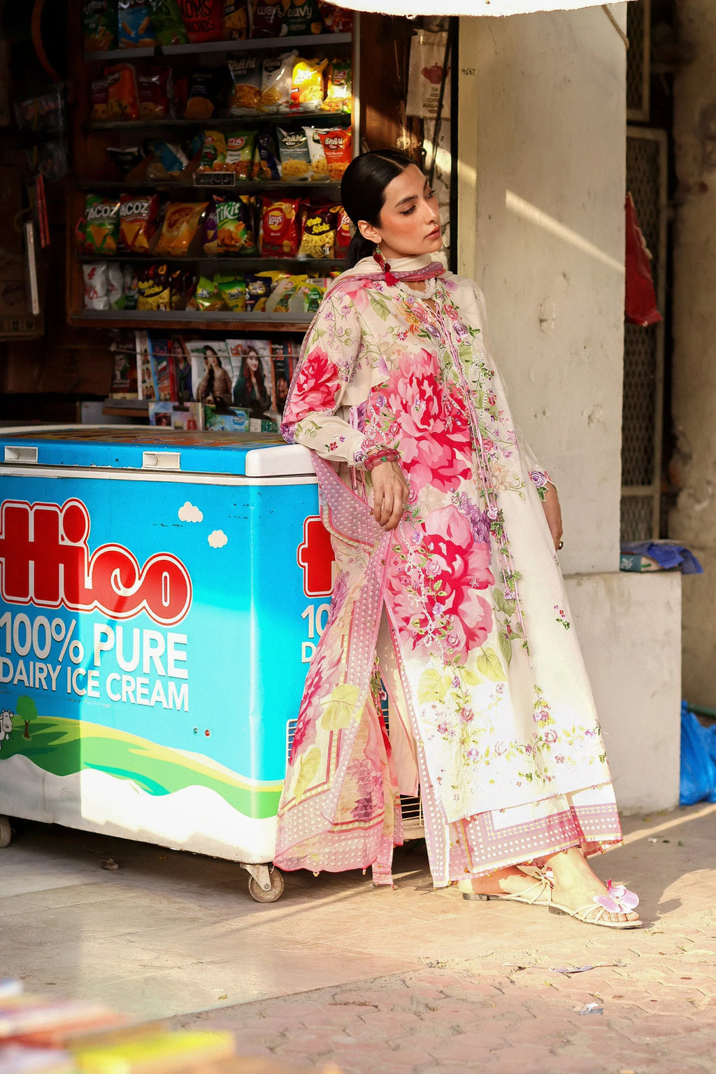 Woman in a floral dress walking past an ice cream cart with a colorful sign.