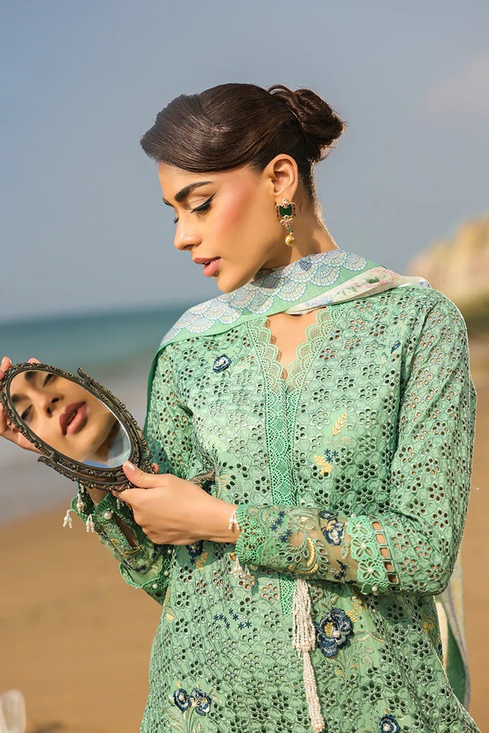 Woman in a green embroidered outfit holding a mirror on a beach.