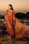 Woman in a traditional embroidered outfit standing on a beach at sunset.