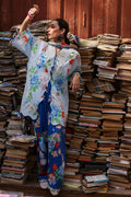 Woman in a floral outfit standing amidst stacks of books with a red wall in the background