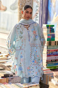 Woman in an embroidered light blue dress standing among books