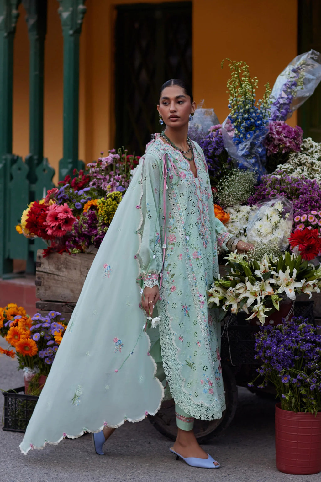 Woman in a light green floral dress standing among colorful flowers.