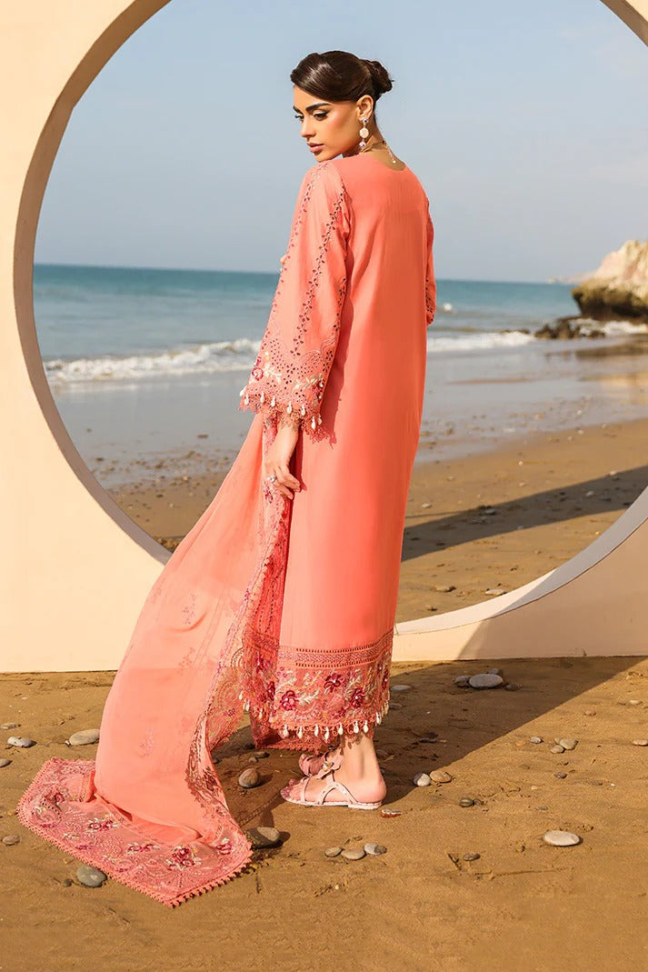 Woman in a pink traditional outfit standing on a beach with ocean view.