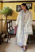 Woman in traditional embroidered outfit standing in a room with yellow walls and a chair.