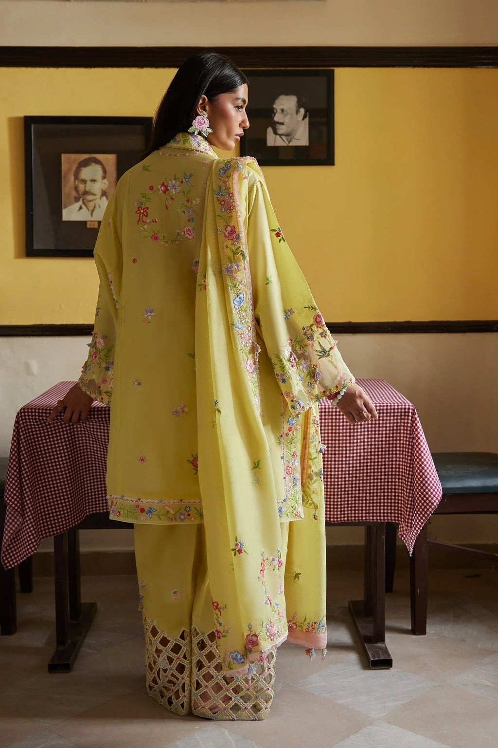 Woman in a yellow traditional outfit standing in a room with framed pictures on the wall.