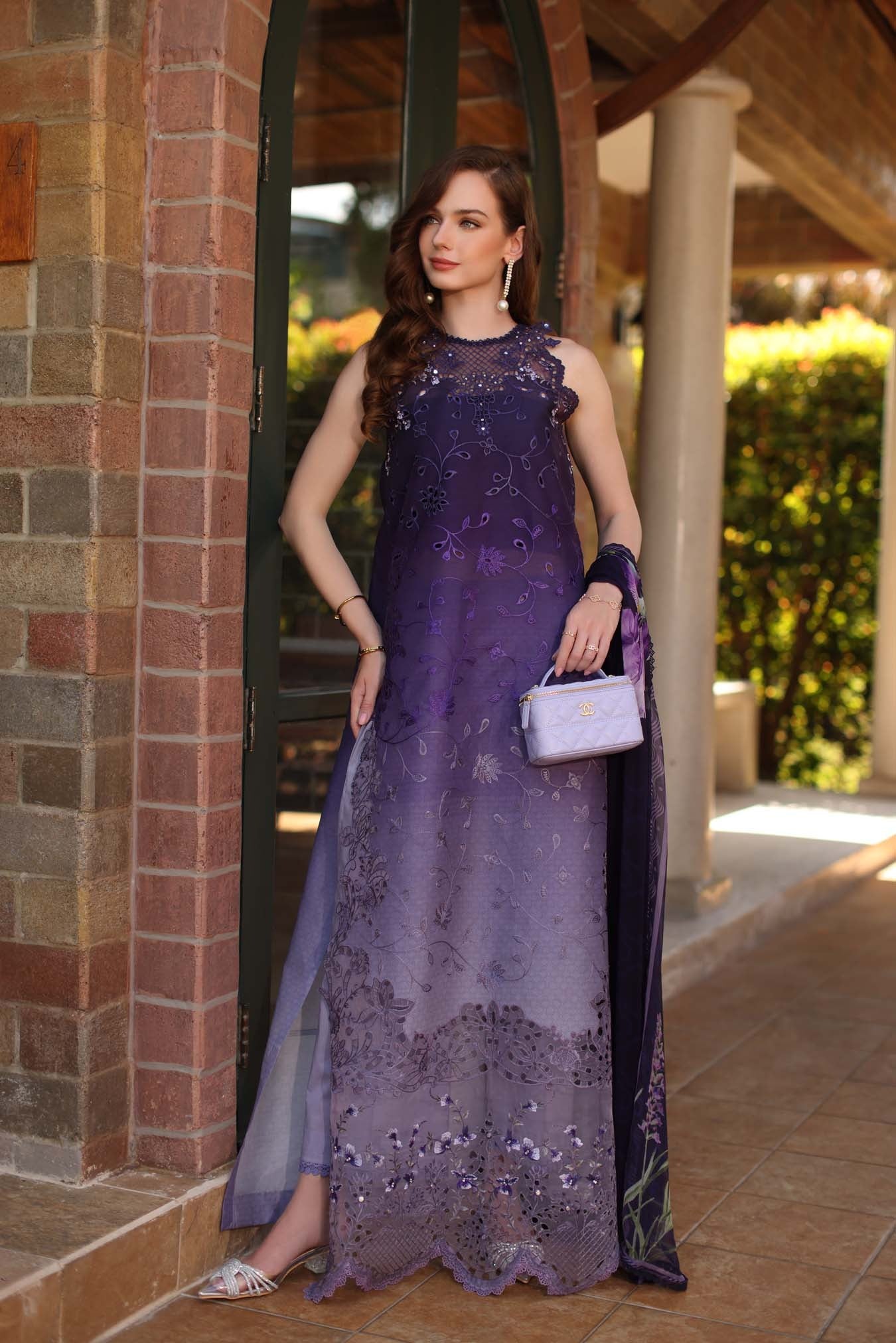 Woman in a purple lace dress standing outdoors near a building entrance.