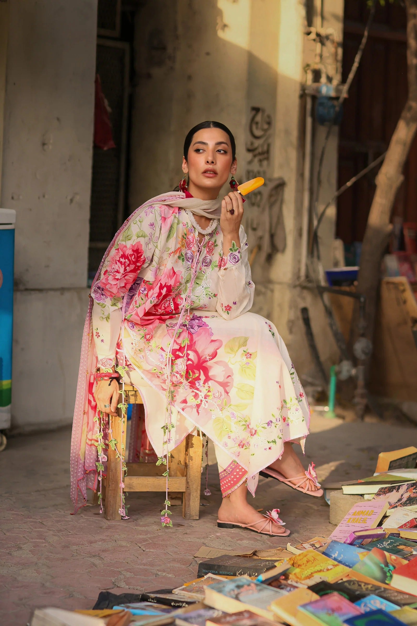 Woman in a colorful floral dress sitting on a stool outdoors with various items around her.