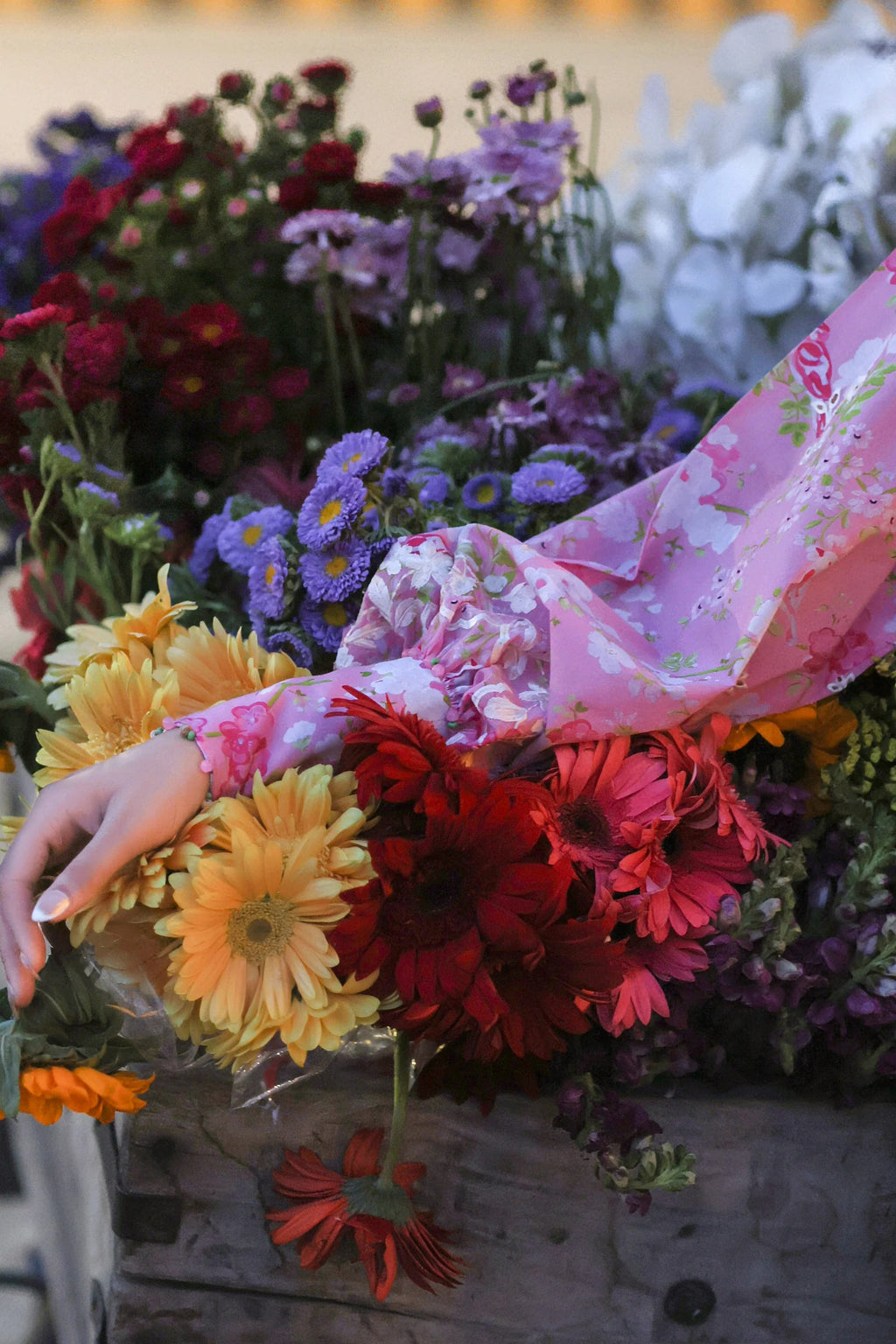 Person holding a bouquet of colorful flowers with a floral-patterned sleeve.