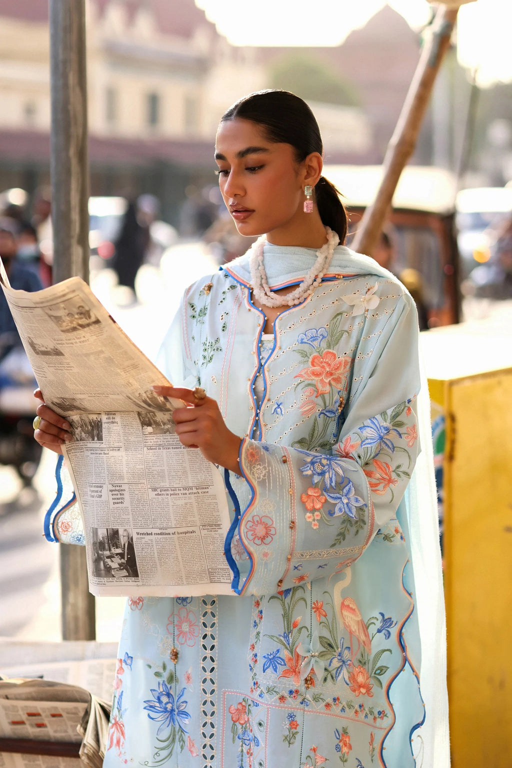 Woman in a floral dress reading a newspaper outdoors.