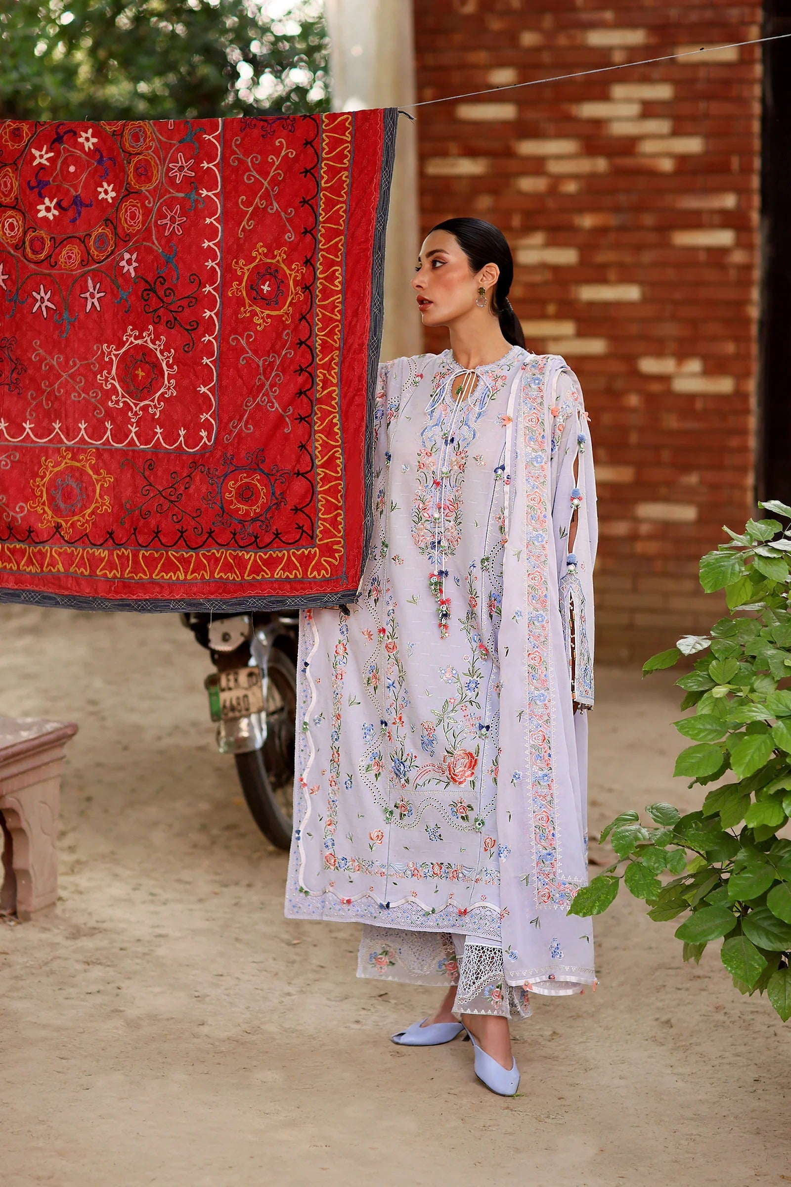 Woman in a white embroidered outfit standing next to a red embroidered fabric outdoors.