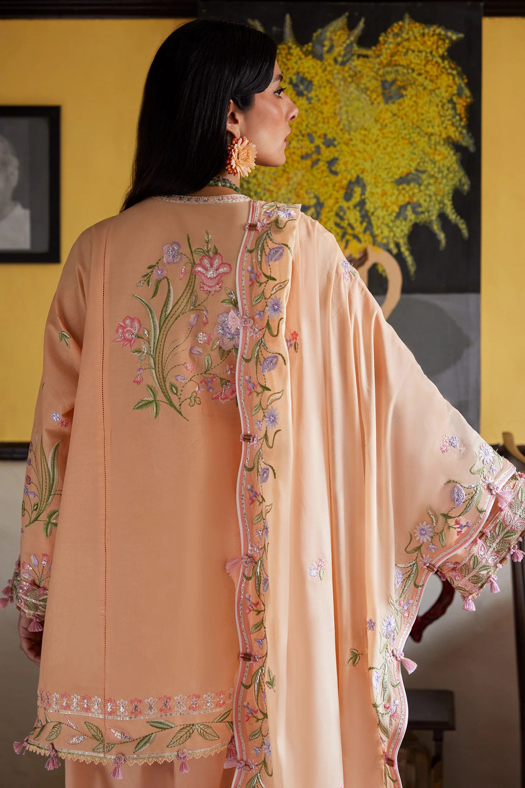 Woman wearing a peach embroidered traditional outfit in a room with a colorful painting on the wall.