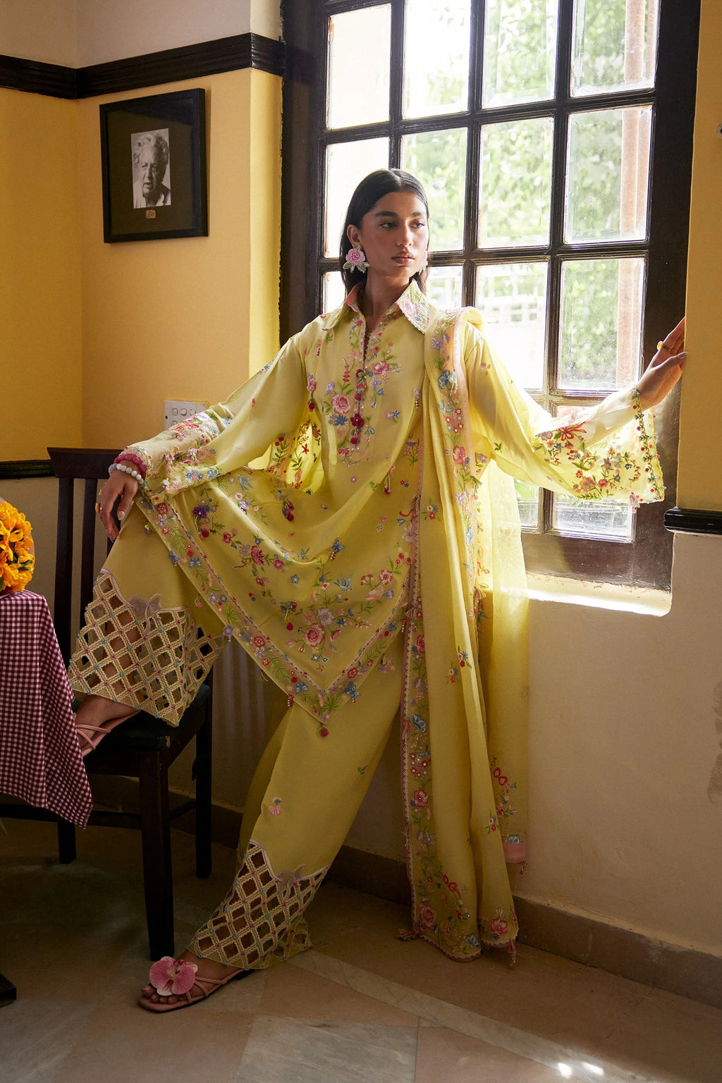 Woman in a yellow traditional outfit standing in a room with a window.