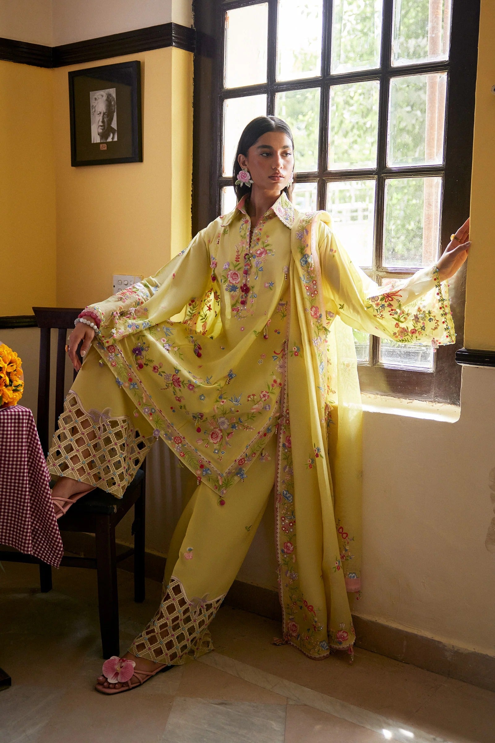 Woman in a yellow traditional outfit standing in a room with a window.