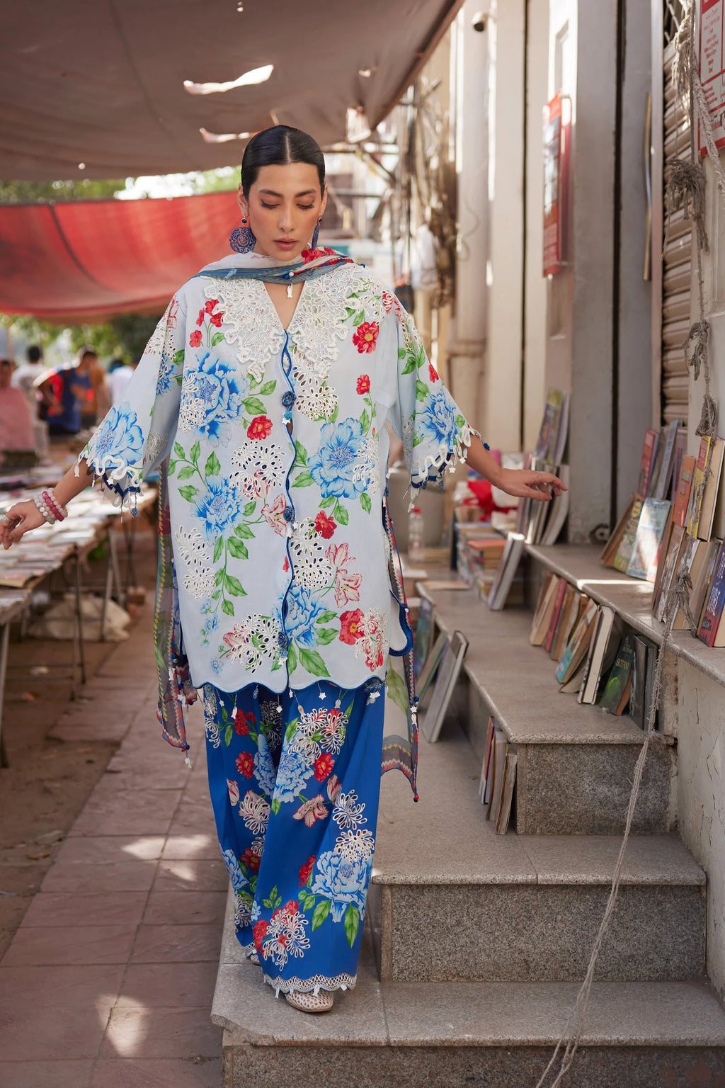 Woman in a floral outfit walking up steps outside a store with books.