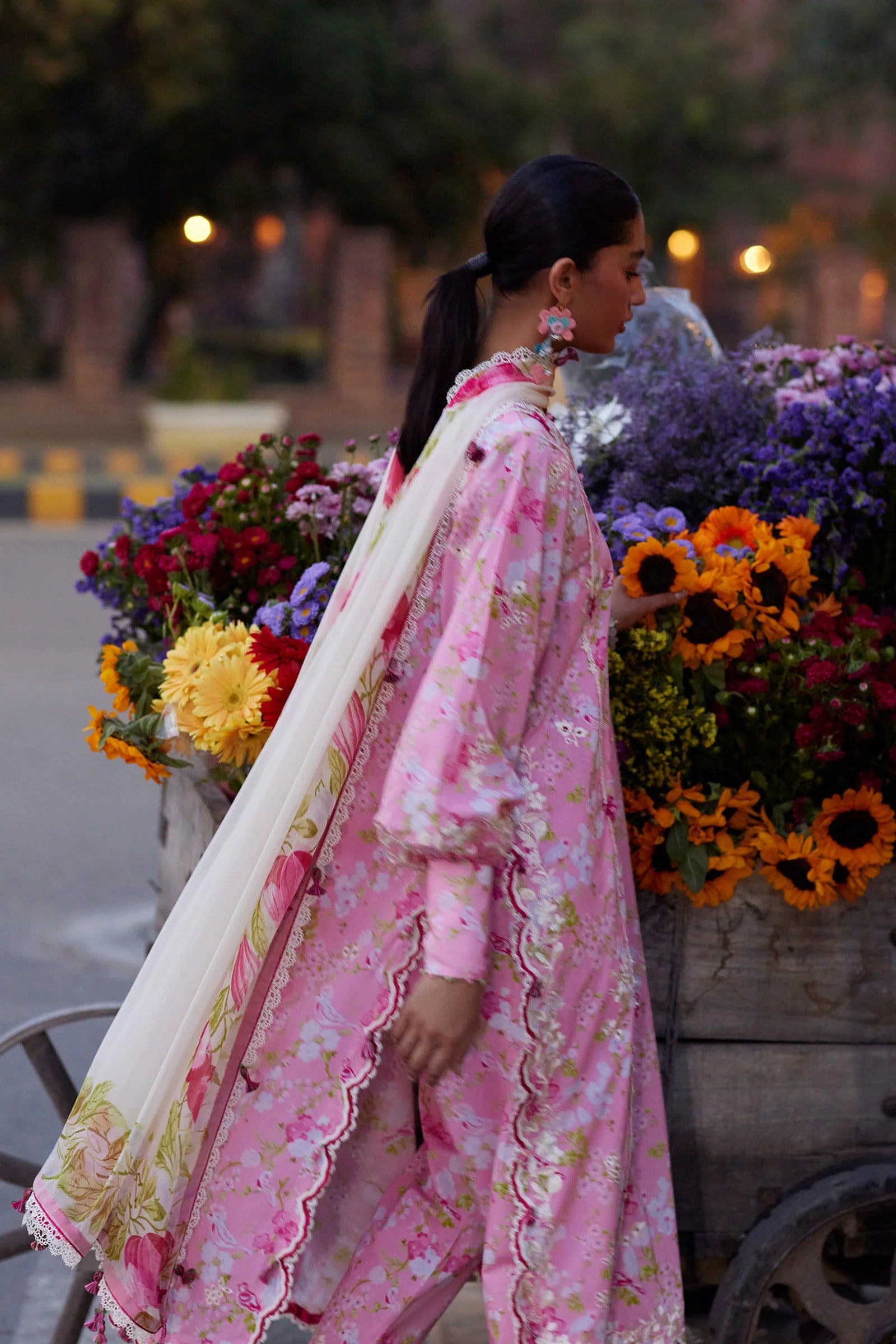 Woman in a pink floral outfit standing next to a cart filled with flowers.