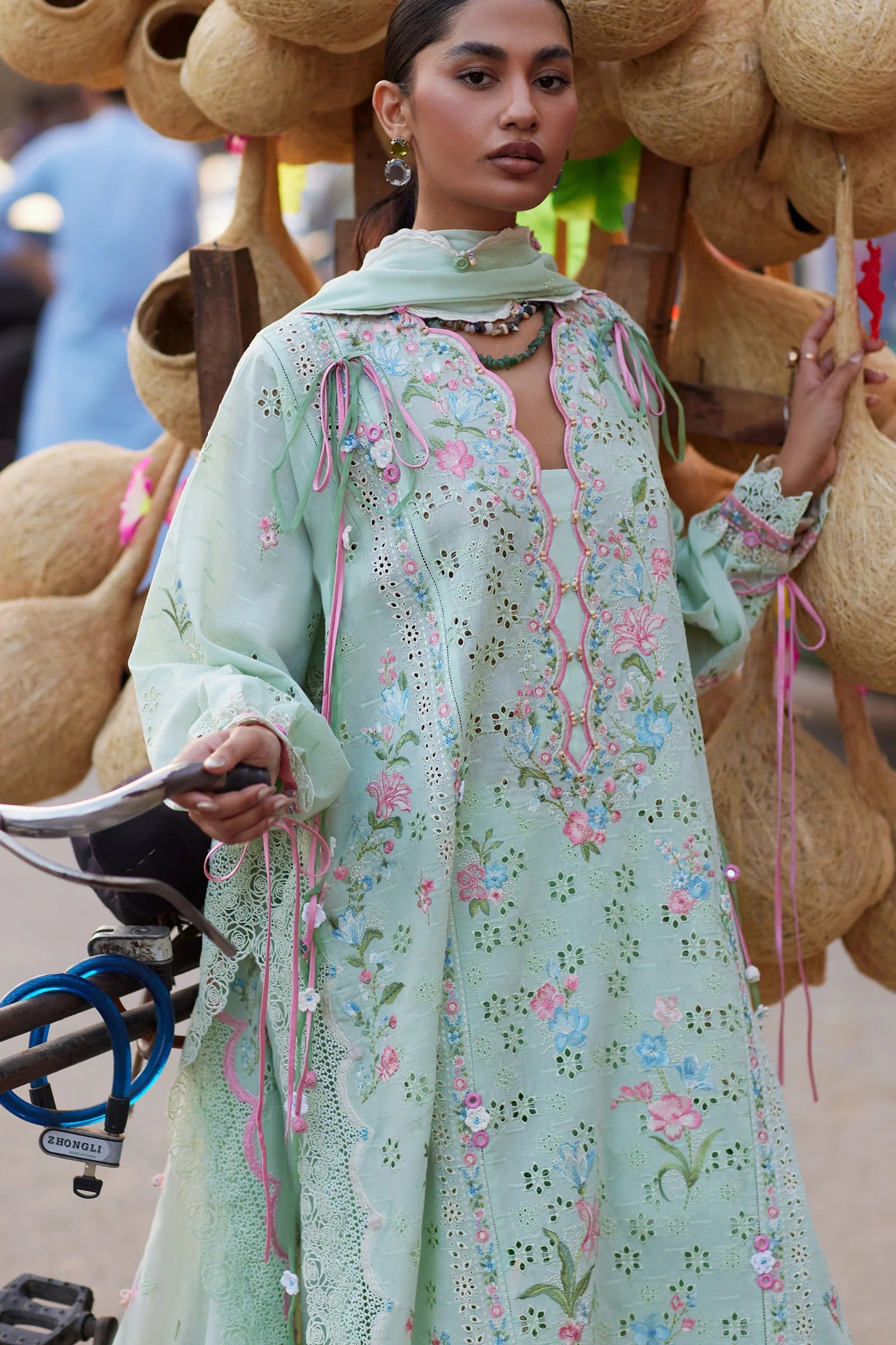 Woman in a light green embroidered dress with floral patterns, standing in front of woven baskets.