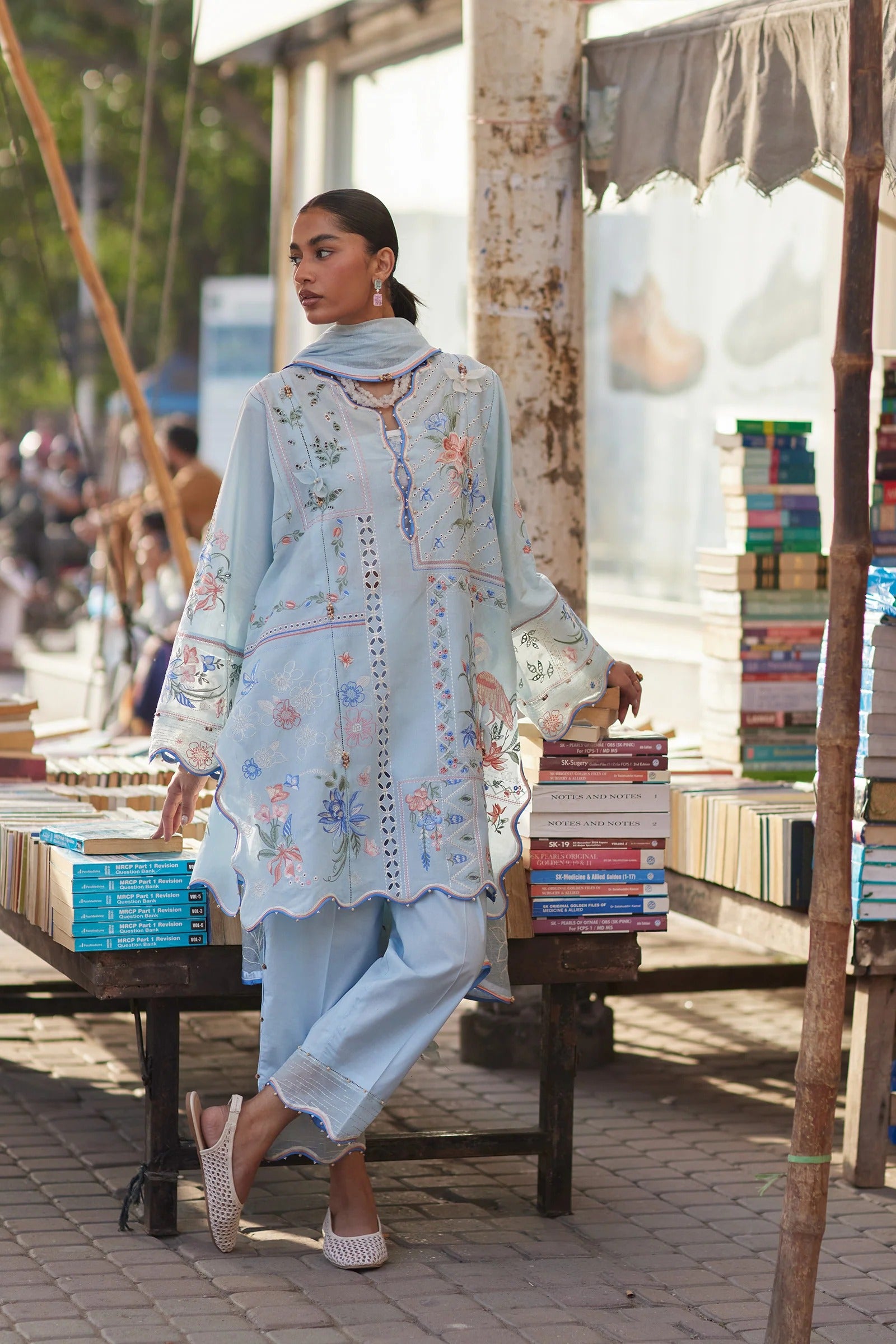 Woman in traditional outfit walking past a book stall at an outdoor market.