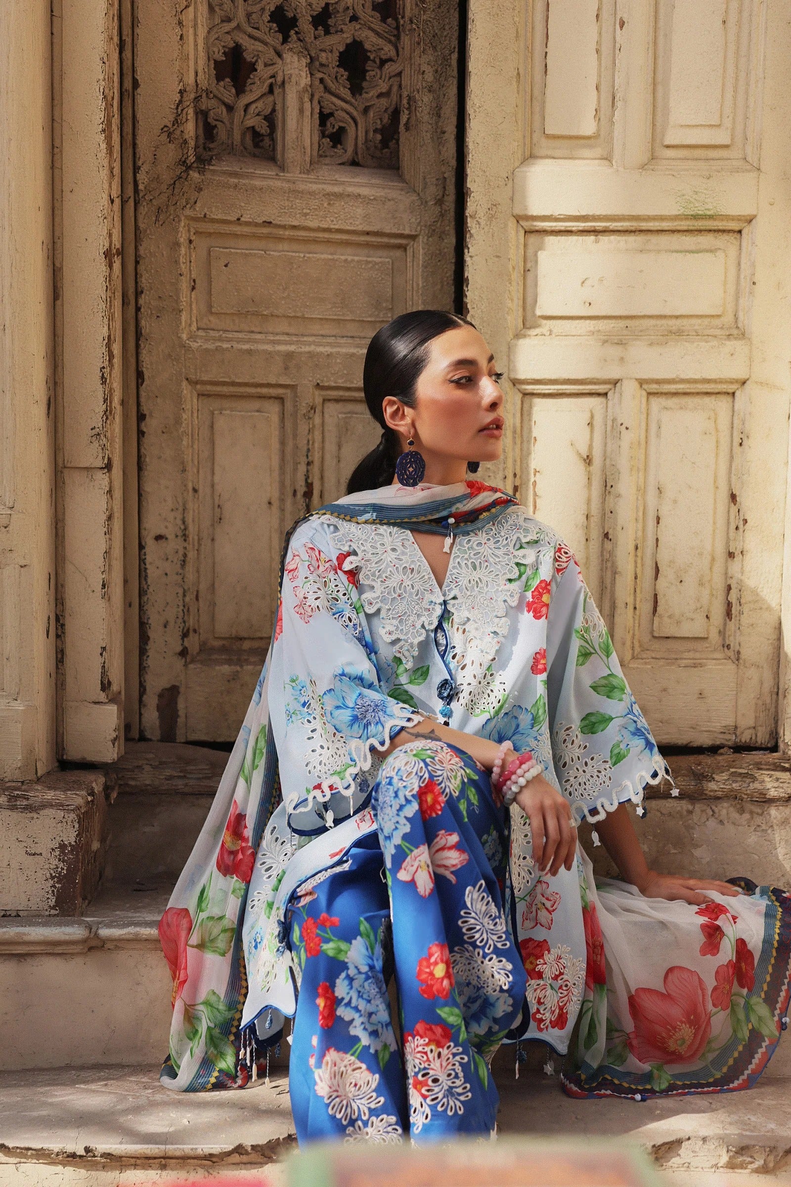 Woman in a floral outfit sitting on steps with a decorative door in the background