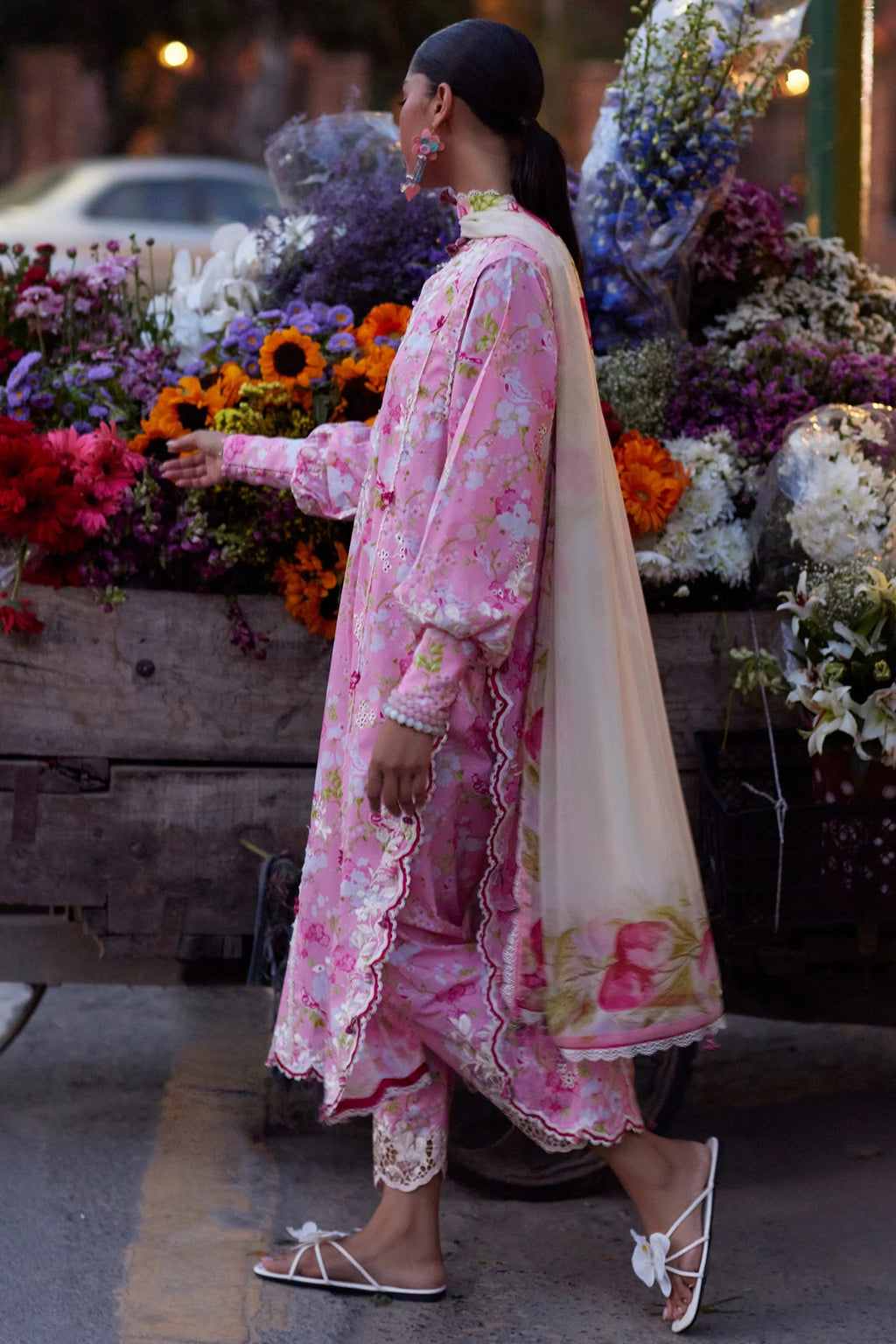 Woman in a pink floral dress standing next to a flower cart at night.