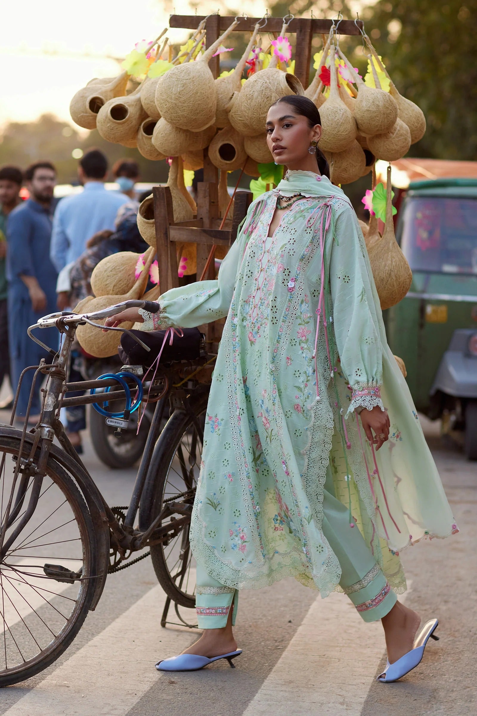 Woman in a light green traditional outfit walking past a street vendor with baskets.