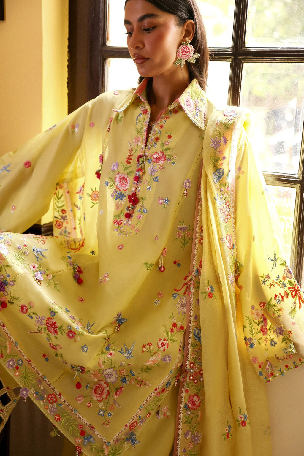 Woman wearing a yellow embroidered traditional outfit in a bright room.
