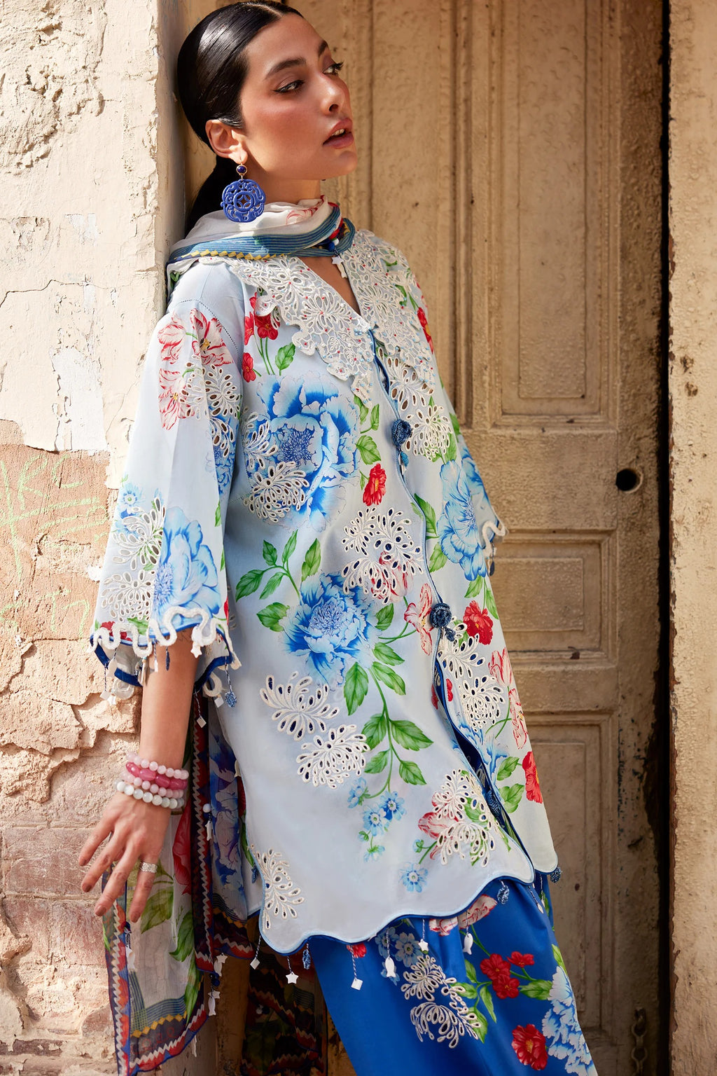Woman in a floral outfit sitting on steps with a decorative door in the background