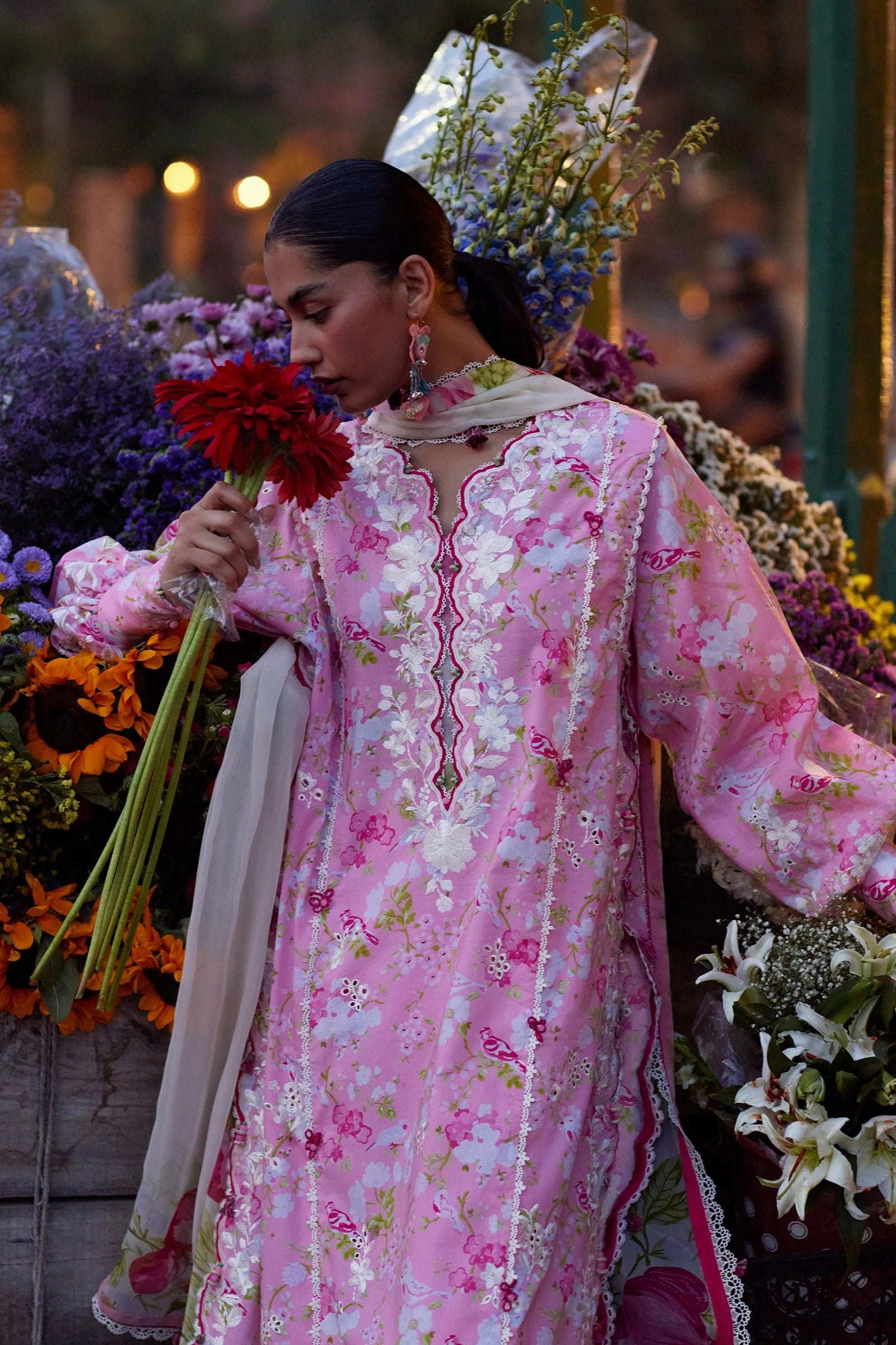 Woman in a pink embroidered outfit holding flowers amidst floral decorations
