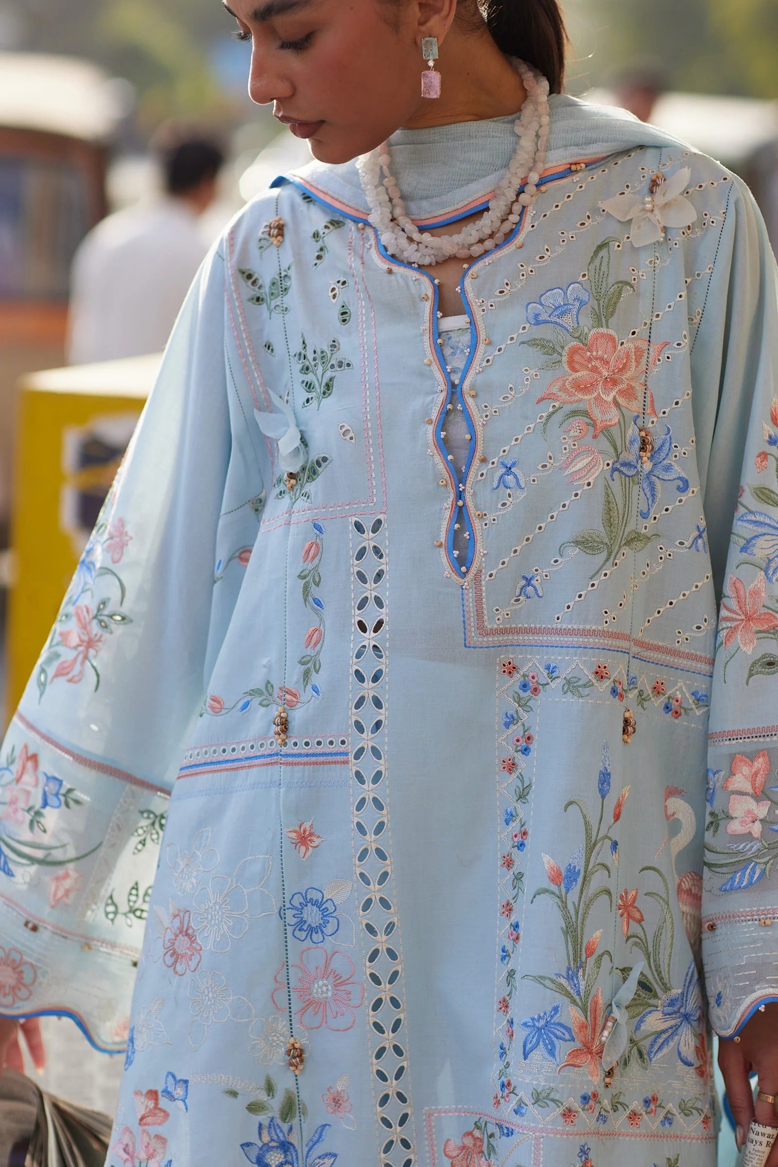 Woman wearing a light blue embroidered traditional outfit with floral patterns.