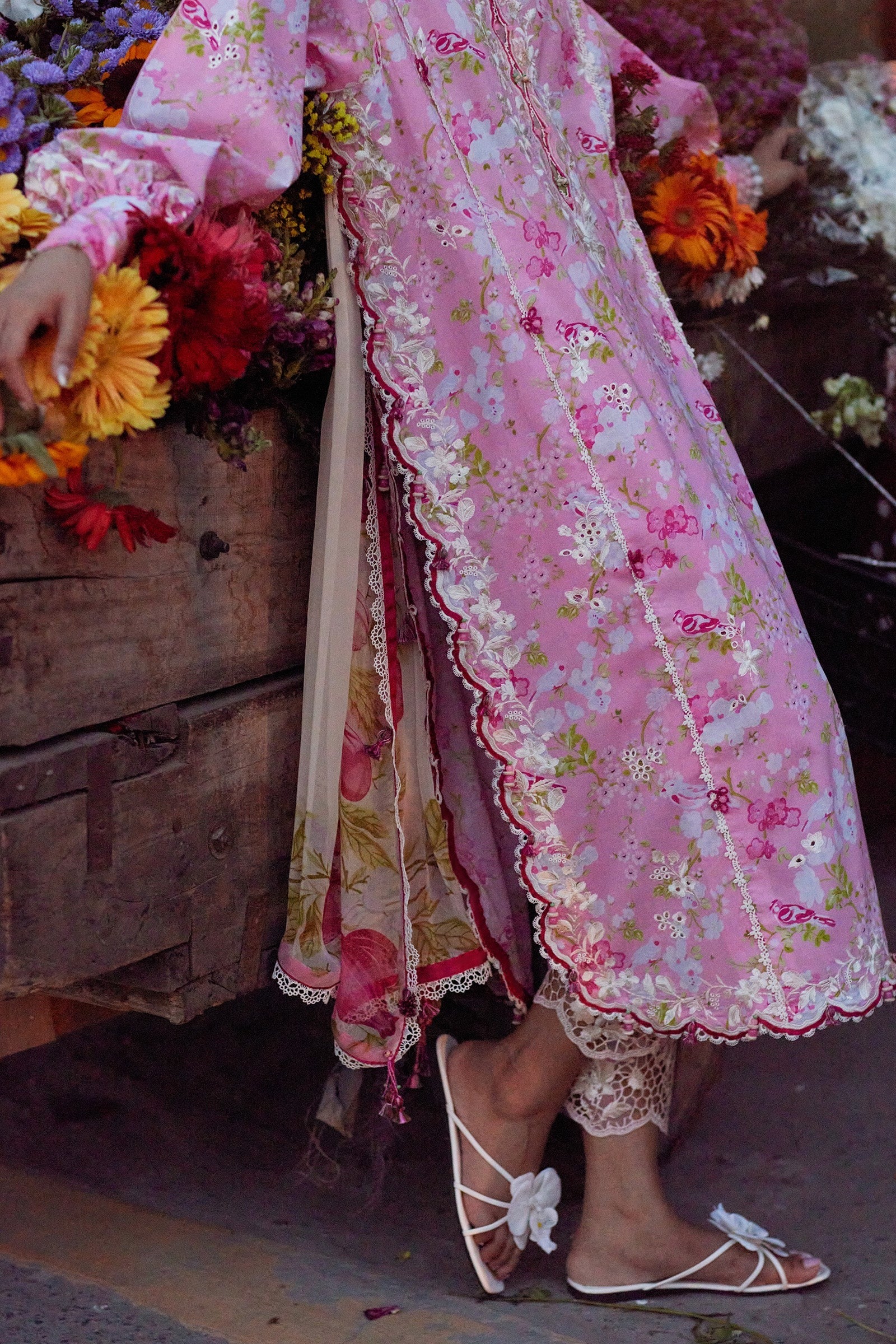 Person wearing a pink floral dress with a wooden cart and flowers in the background
