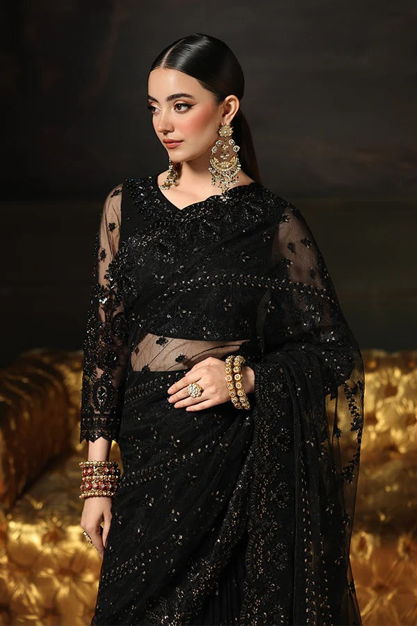 Woman wearing a black saree with gold jewelry against a dark background