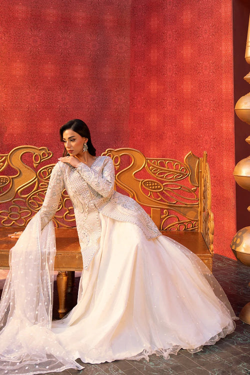 Woman in a white traditional outfit sitting on an ornate chair against a red wall.