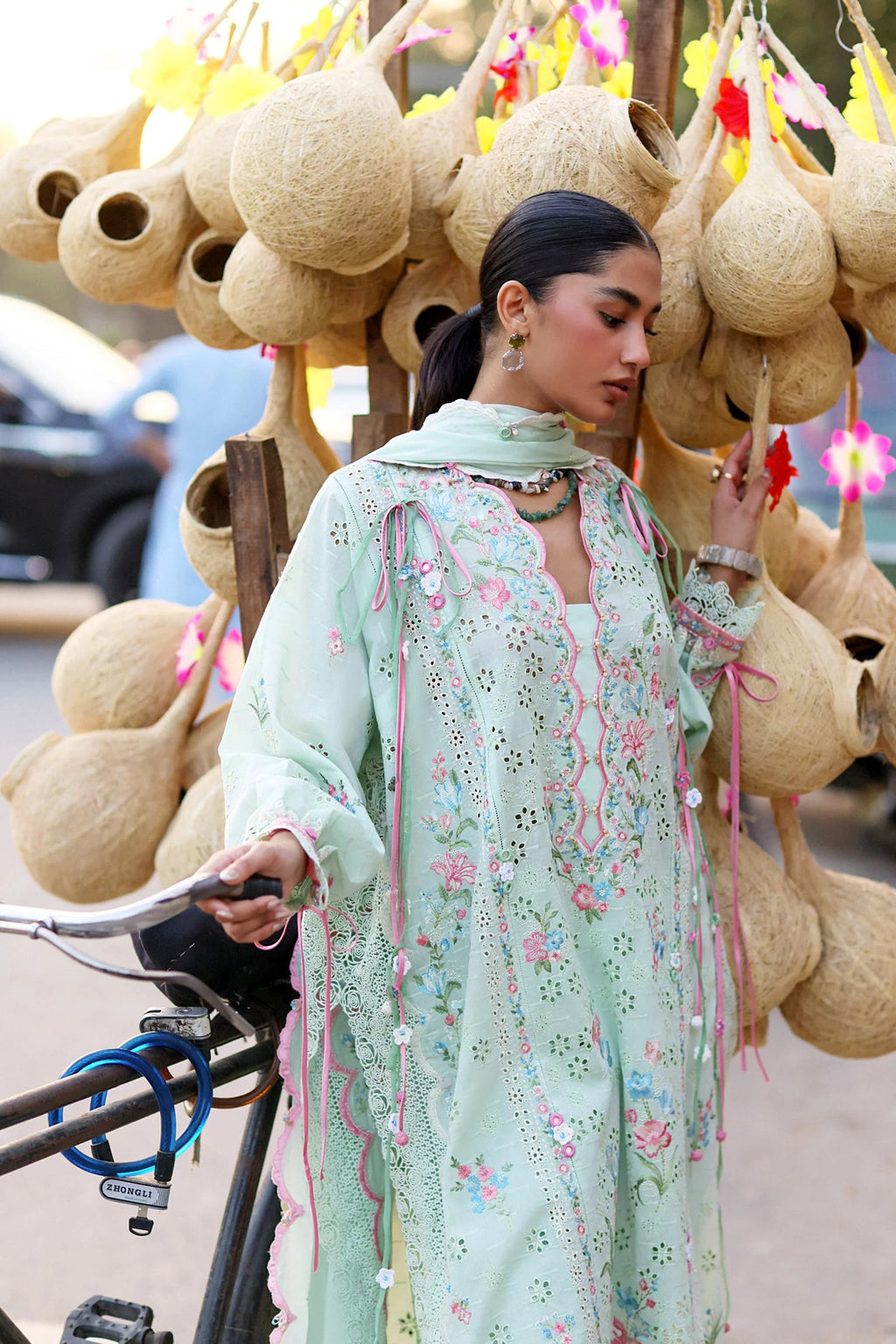 Woman in a light green floral dress standing next to a cart with gourd-like objects.