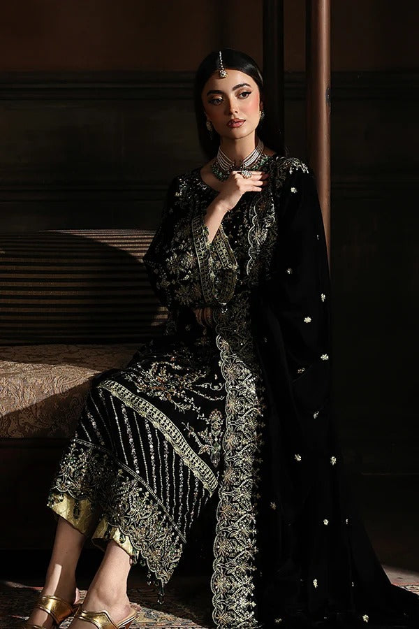 Woman in a black and gold traditional outfit with intricate patterns in a dimly lit room.