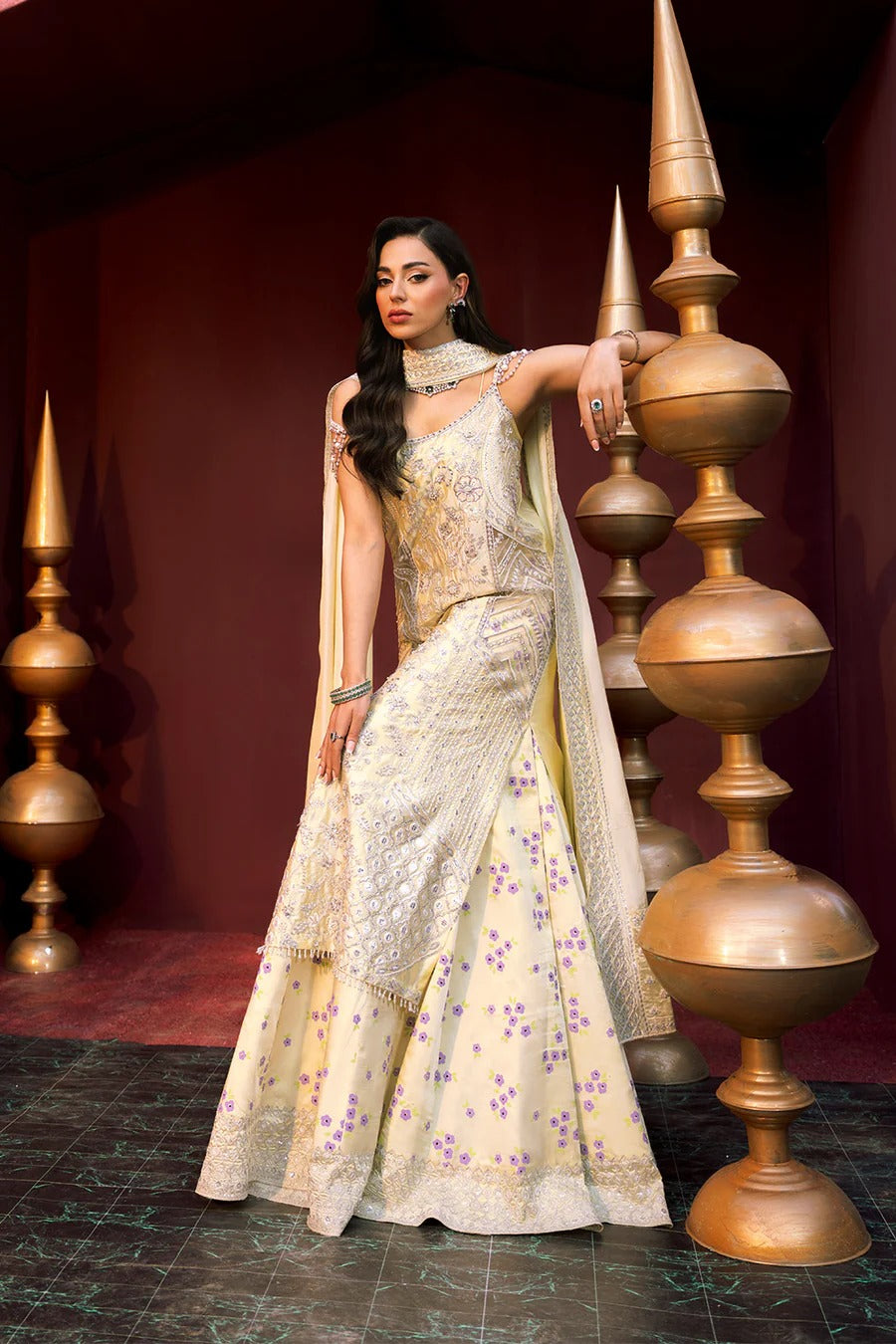 Woman in a traditional outfit standing next to decorative gold pots against a dark background