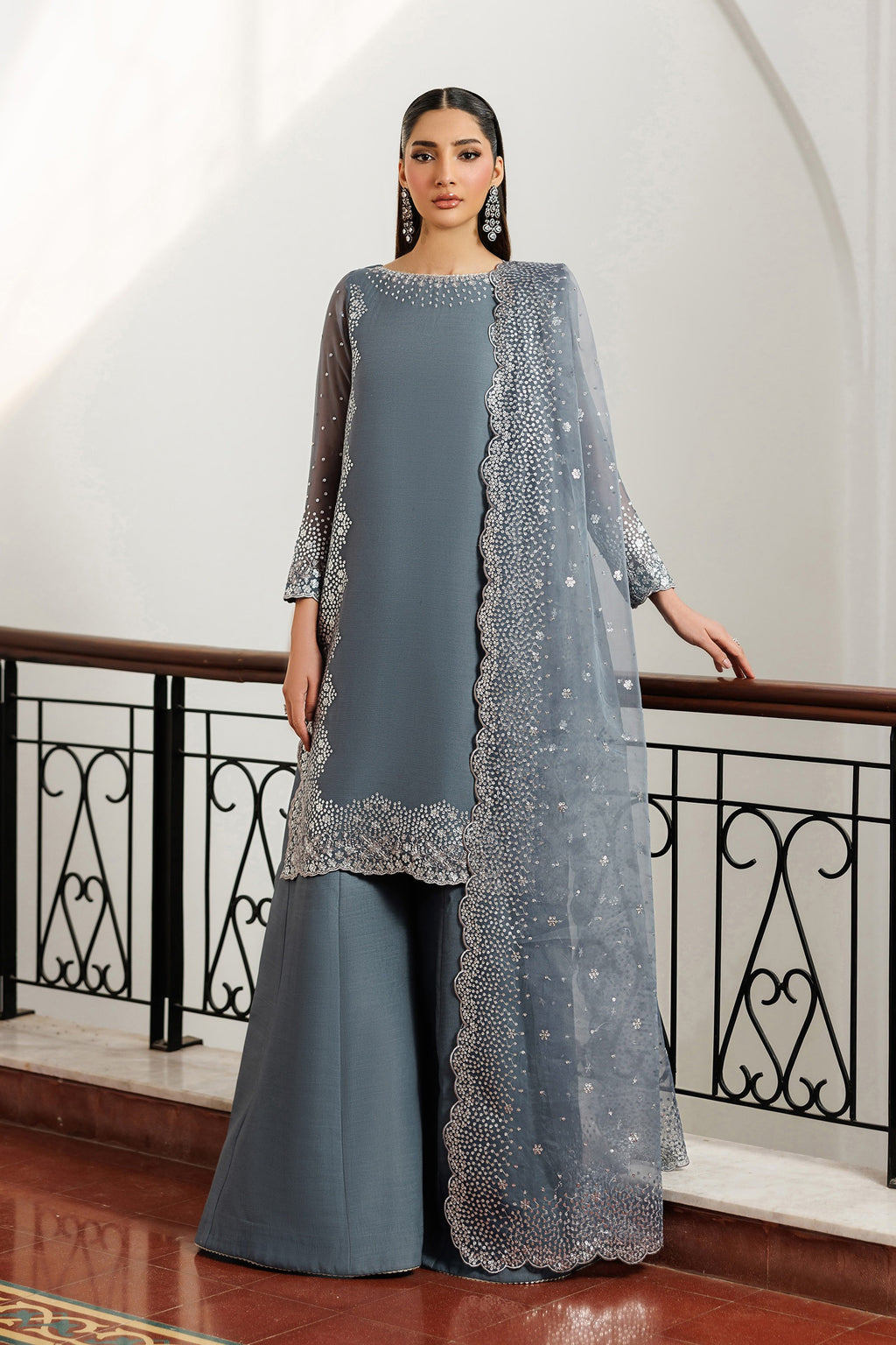 Woman wearing a gray traditional outfit with a matching dupatta in an elegant indoor setting.