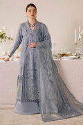 Woman in a light blue embroidered traditional outfit standing in a decorated room.