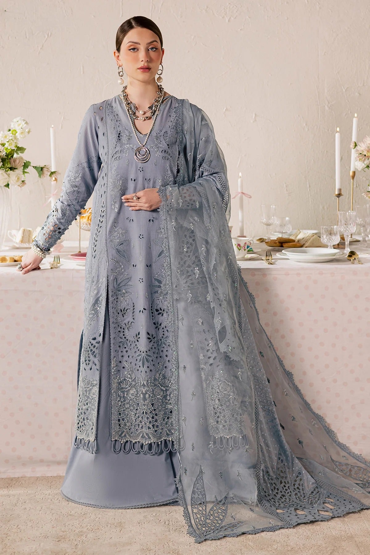 Woman in a light blue embroidered traditional outfit standing in a decorated room.