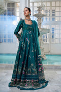 Woman in a teal embroidered dress standing in a decorative interior setting.